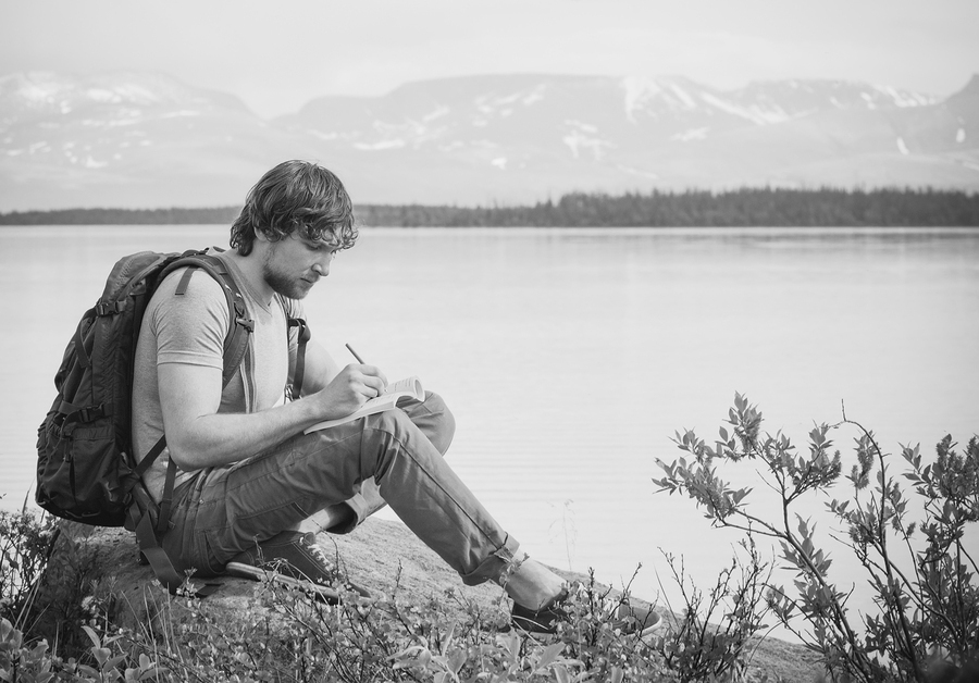 Young Man Traveler with backpack reading book and writing notes